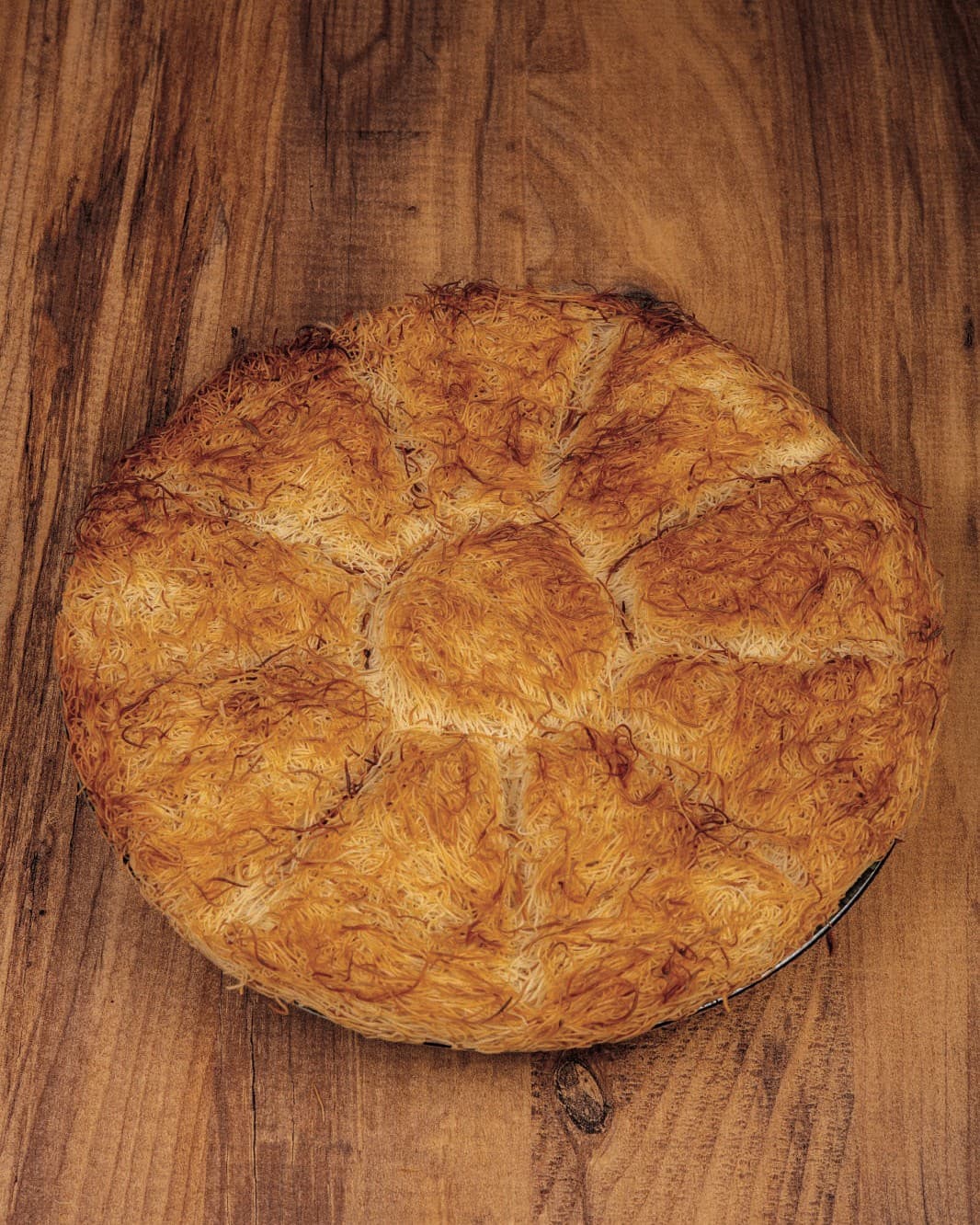 A round, golden carrot-slice kadayif dessert on a wooden table