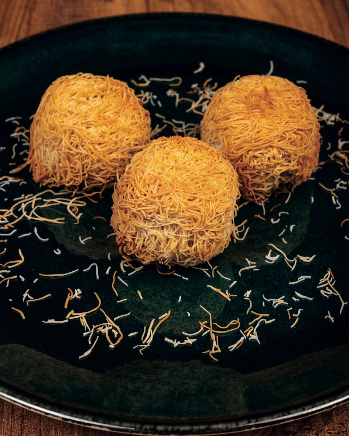 Three round portions of rolled kadayif on a dark plate